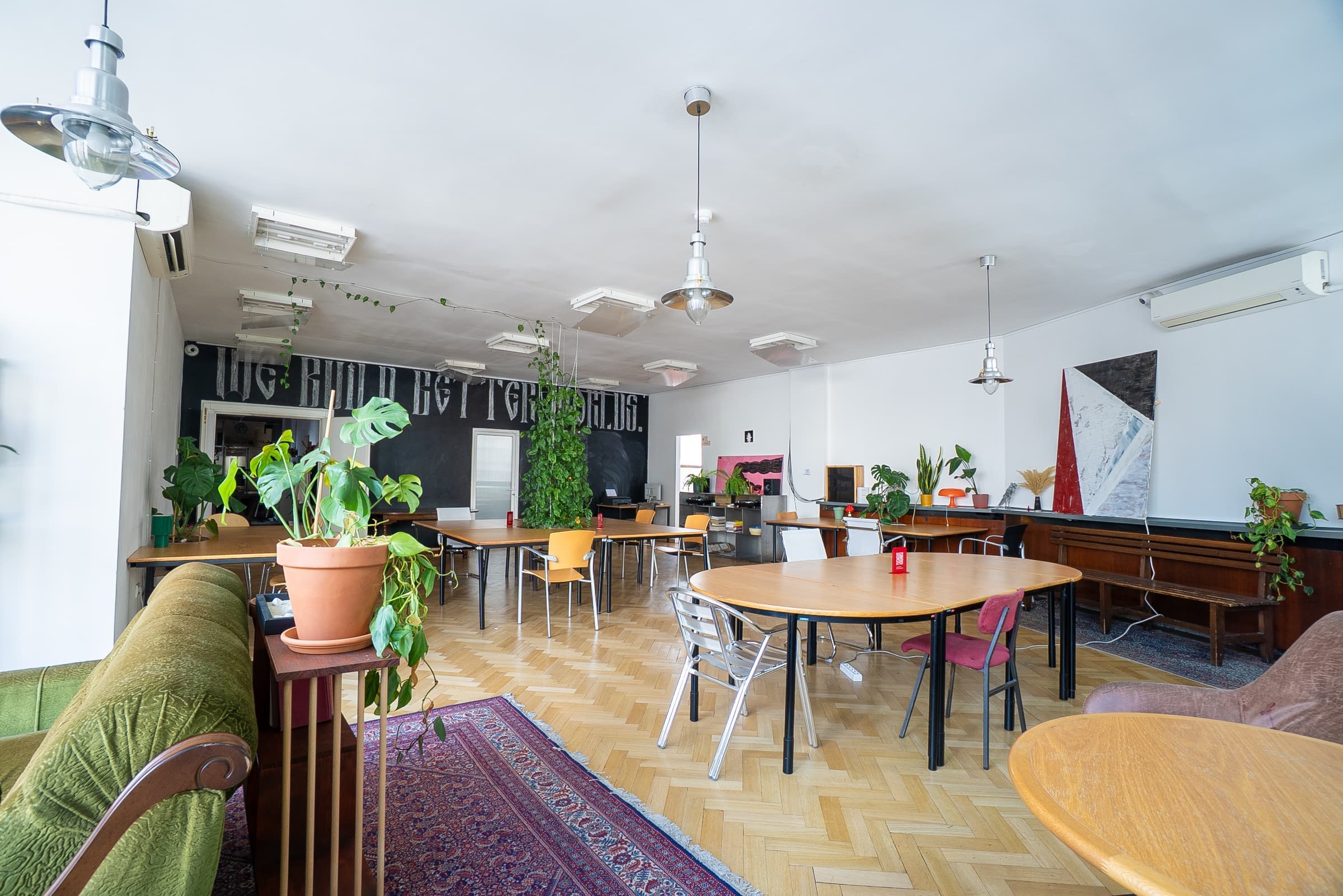 Open-plan coworking floor at SENSE—S.SPACE with shared tables, chalkboard wall, and climbing plants