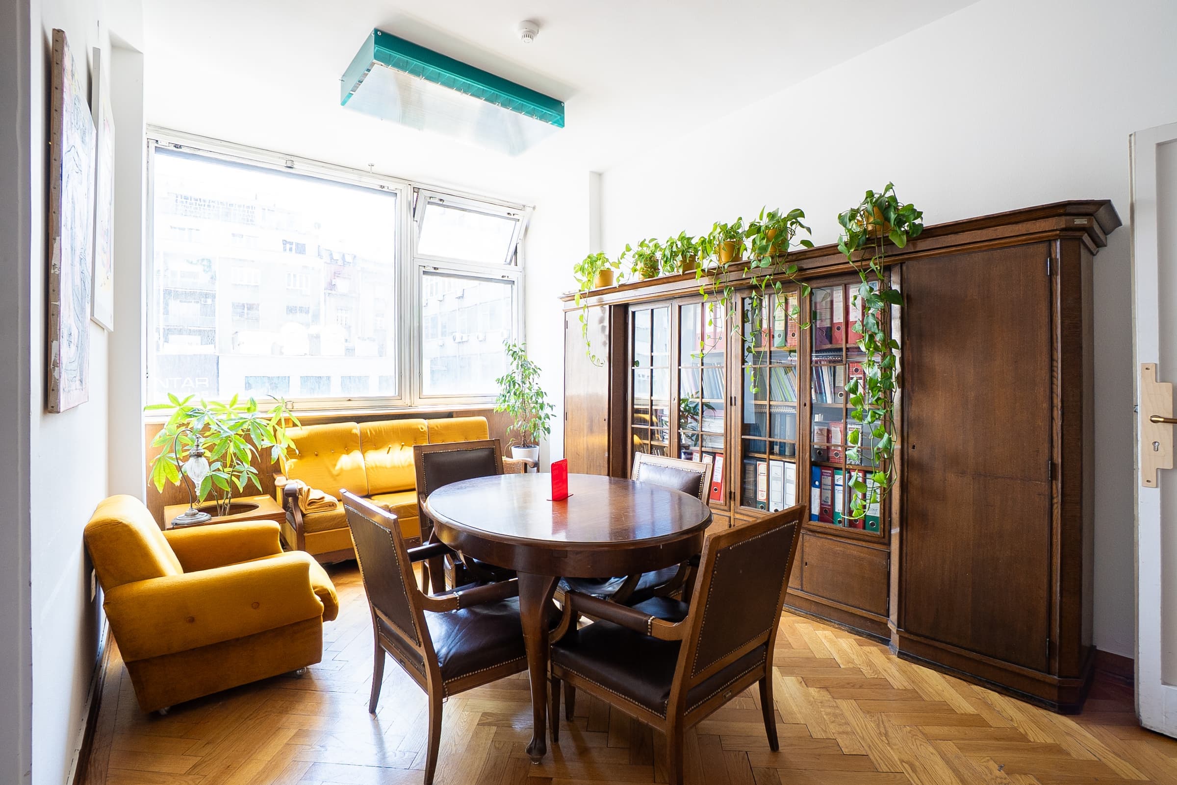 Sunlit meeting nook at SENSE—S.SPACE with round table, yellow velvet seating, and vintage bookcase