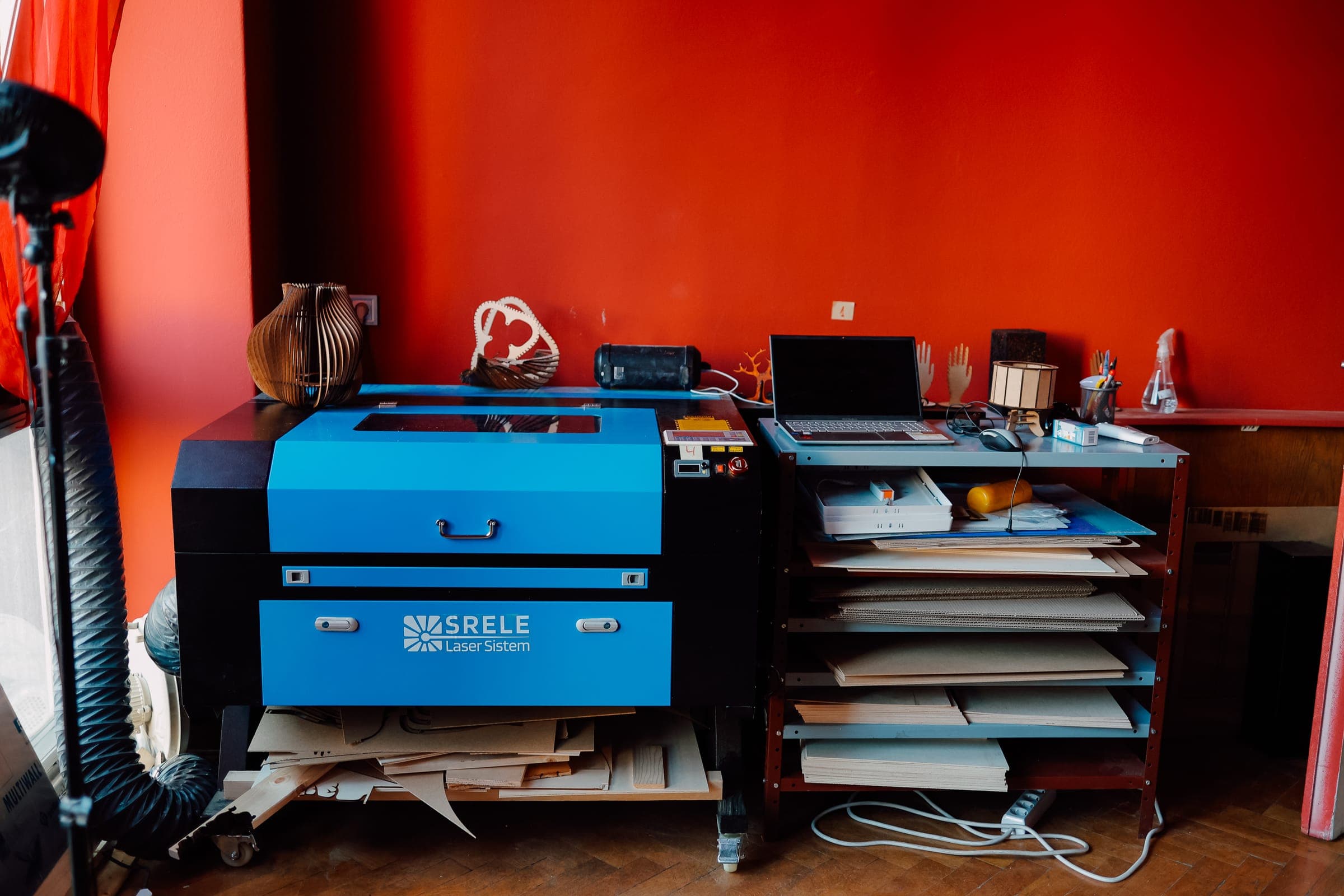 Laser-cutting room at SENSE—S.SPACE with SRELE cutter, laptop workstation, and wooden prototypes